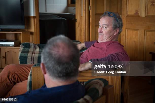 two middle-aged men sitting in a lounge room having a discussion. - mooloolaba stock-fotos und bilder