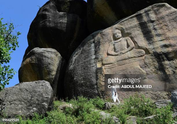 This photo taken on April 26, 2018 shows a Pakistani visitor walking past a seventh-century rock sculpture of a seated Buddha carved into a mountain...