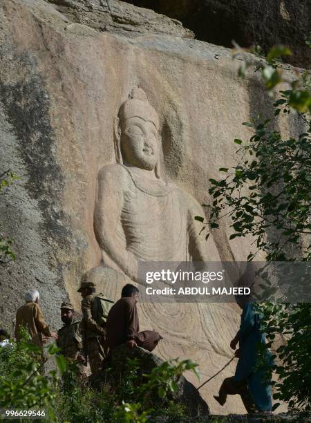 This photo taken on April 26, 2018 shows Pakistani visitors standing next to the seventh-century rock sculpture of a seated Buddha carved into a...