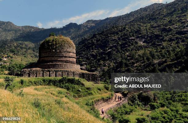 This photo taken on April 27, 2018 shows Pakistani visitors walking past a centuries-old stupa, a dome-shaped Buddhist monument, in the town of Amluk...