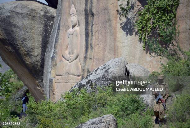 This photo taken on April 26, 2018 shows a Pakistani soldier walking past the seventh-century rock sculpture of a seated Buddha carved into a...