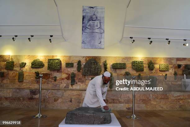 This photo taken on April 27, 2018 shows a worker cleaning a rock with images of Buddha's feet at a museum in the town of Mingora, the capital of...
