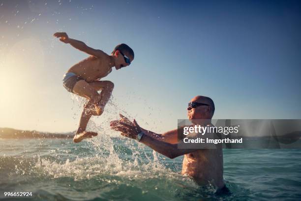 senior man playing with grandson in sea - life si a beach imagens e fotografias de stock