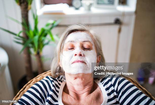 senior woman with facial mask sitting on the chair at home. top view. - halfpoint stockfoto's en -beelden