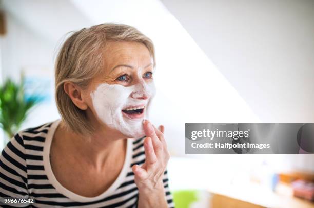 senior woman applying facial mask at home. copy space. - halfpoint stock-fotos und bilder