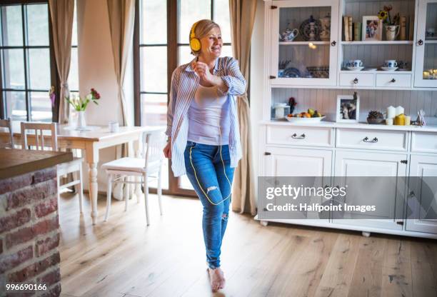 senior woman with yellow headphones listening to music and dancing at home. - halfpoint stock-fotos und bilder