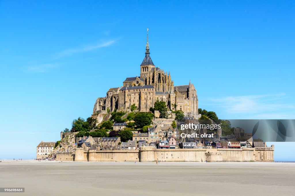 Gesamtansicht der Gezeiten Insel Mont Saint-Michel, befindet sich in Frankreich an der Grenze zwischen Normandie und Bretagne, mit dem exponierten Sand der Bucht bei Ebbe im Vordergrund unter blauem Himmel.