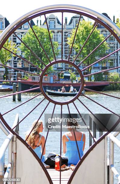 two happy young women talking on the amstel river pier. - canal house stock pictures, royalty-free photos & images