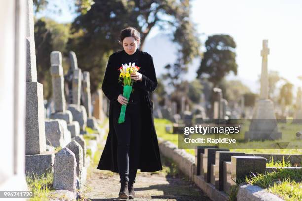 bereaved young woman in black taking flowers to grave - graveyard stock pictures, royalty-free photos & images