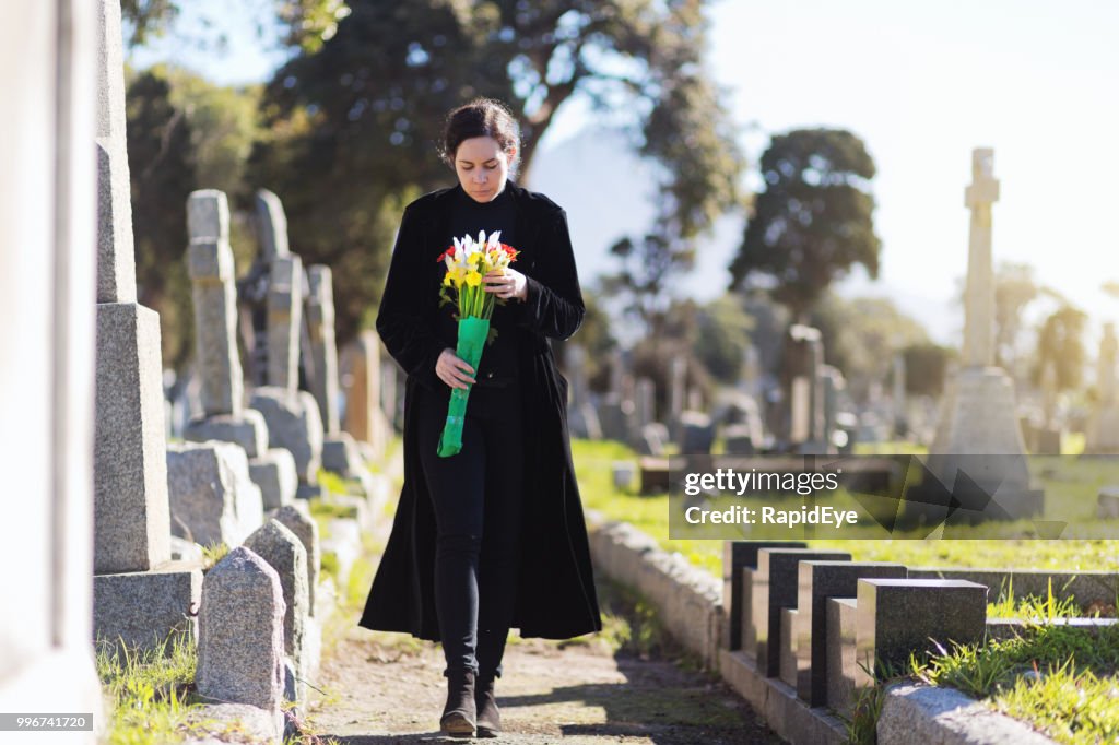 Jovem mulher de negro levar flores ao túmulo de luto