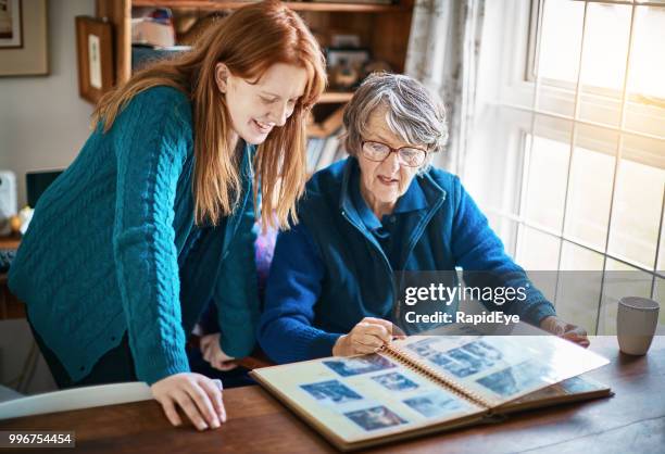 old lady shows her smiling granddaughter the family photo album - winter testing imagens e fotografias de stock