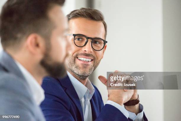rijpe zakenman glimlachend in vergadering - izusek stockfoto's en -beelden