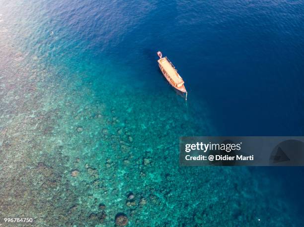 aerial view of a wooden boat at the limit of the coral reef in amed bay in north bali in indonesia - didier marti stock pictures, royalty-free photos & images