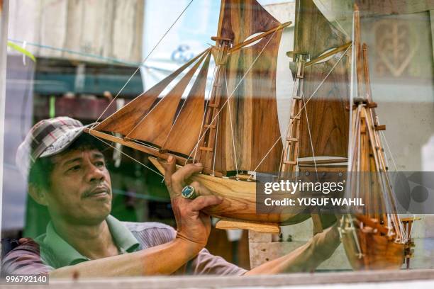 This picture taken on July 8, 2018 shows a man holding a replica of a traditional Pinisi boat in Tana Beru, on Indonesia's South Sulawesi island. -...