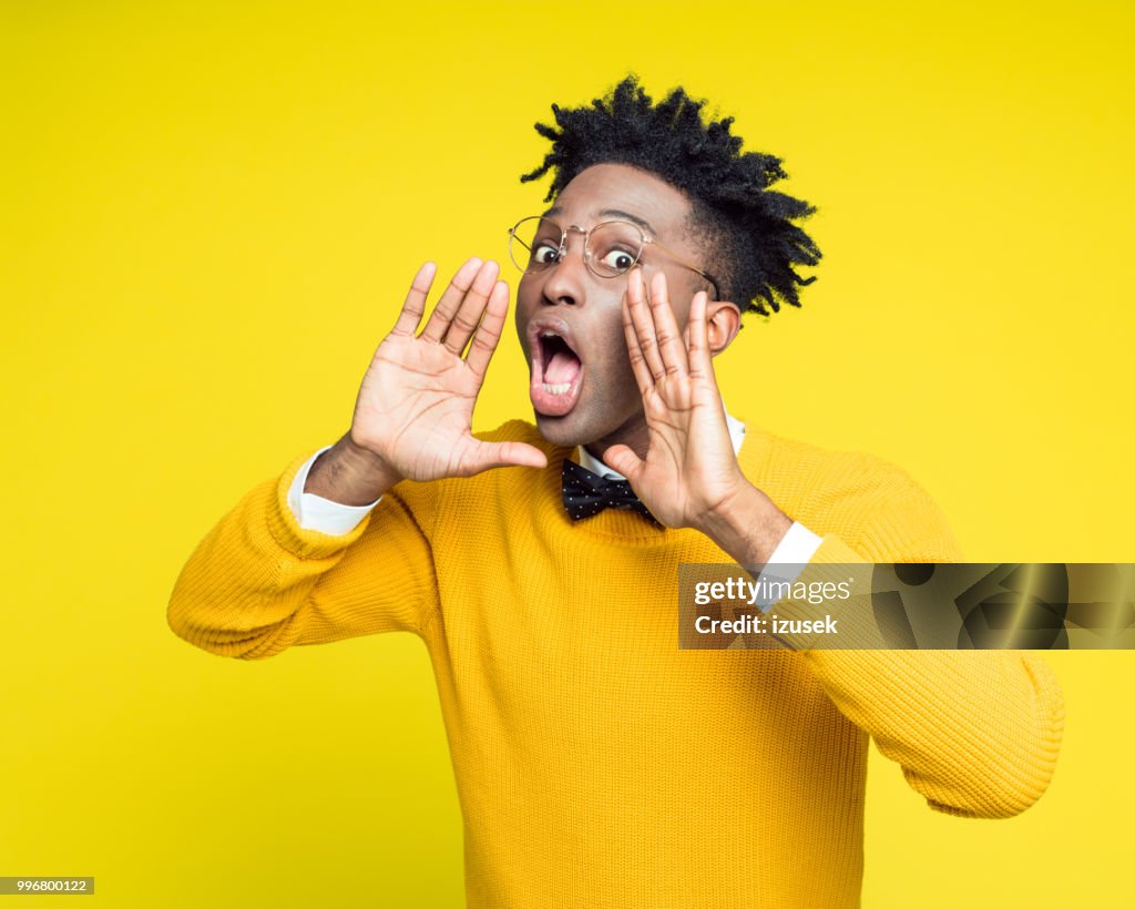 Portrait of nerdy young man shouting against yellow background