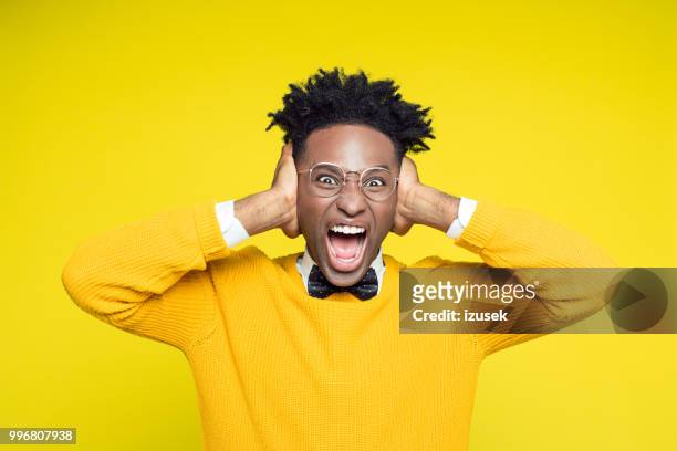 portrait of angry nerdy young man shouting against yellow background - izusek stock pictures, royalty-free photos & images