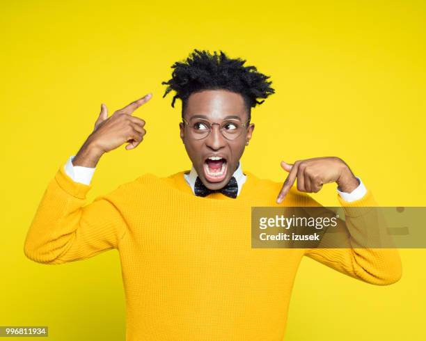 portrait of angry nerdy young man gesturing against yellow background - izusek stock pictures, royalty-free photos & images
