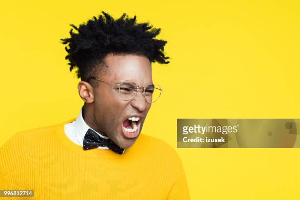 porträt von wütend nerdy junge mann schreien vor gelbem hintergrund - izusek stock-fotos und bilder
