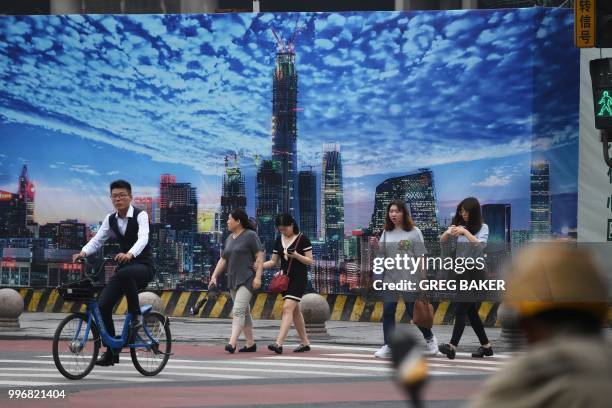 People cross a road in front of a billboard on the wall of a construction site in Beijing's central business district on July 12, 2018.