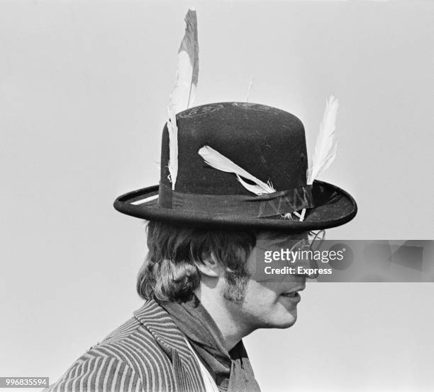 John Lennon , guitarist and singer with the Beatles, pictured wearing hat with feathers attached during filming of 'Magical Mystery Tour' in a field...