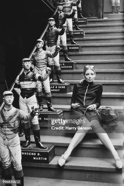 English fashion model Jane Lumb pictured seated on a staircase beside lawn jockey statues at the 21 Club in New York on 4th October 1967.