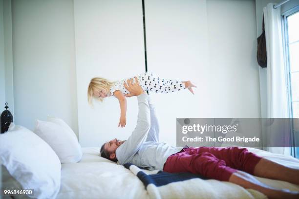 man holding daughter in air while lying in bed - blonde fille photos et images de collection