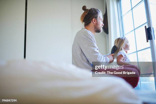 father combing his daughter's hair by window in bedroom - man hair bun fotografías e imágenes de stock
