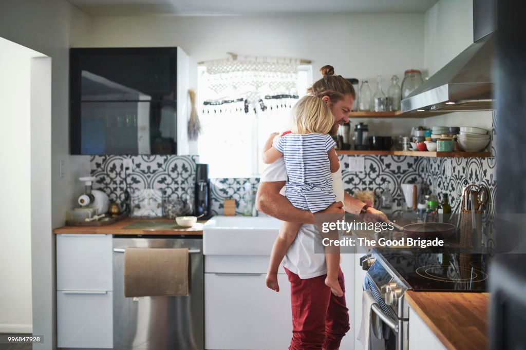 Mid adult father carrying daughter while cooking food in kitchen