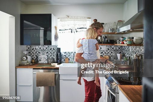 Mid adult father carrying daughter while cooking food in kitchen Mid adult father carrying daughter while cooking food in kitchen