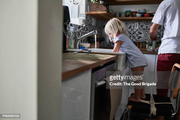 girl washing dishes at kitchen sink while father cooks breakfast - sherman oaks fotografías e imágenes de stock