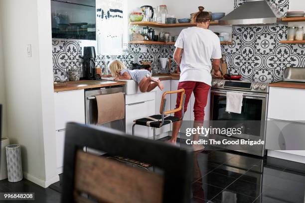 mid adult father cooking food with playful girl in kitchen at home - hipster in a kitchen stock-fotos und bilder