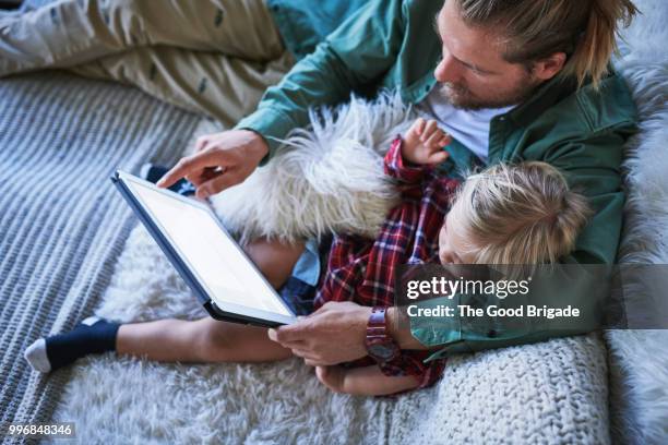 father and daughter using digital tablet on living room sofa - tablet screen home stock-fotos und bilder