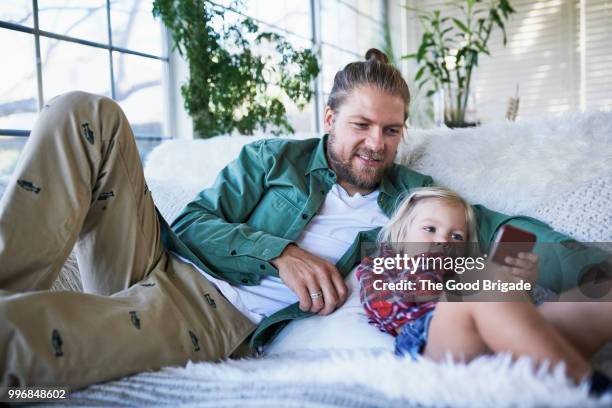 mid adult father looking at daughter using mobile phone on sofa at home - sherman oaks fotografías e imágenes de stock