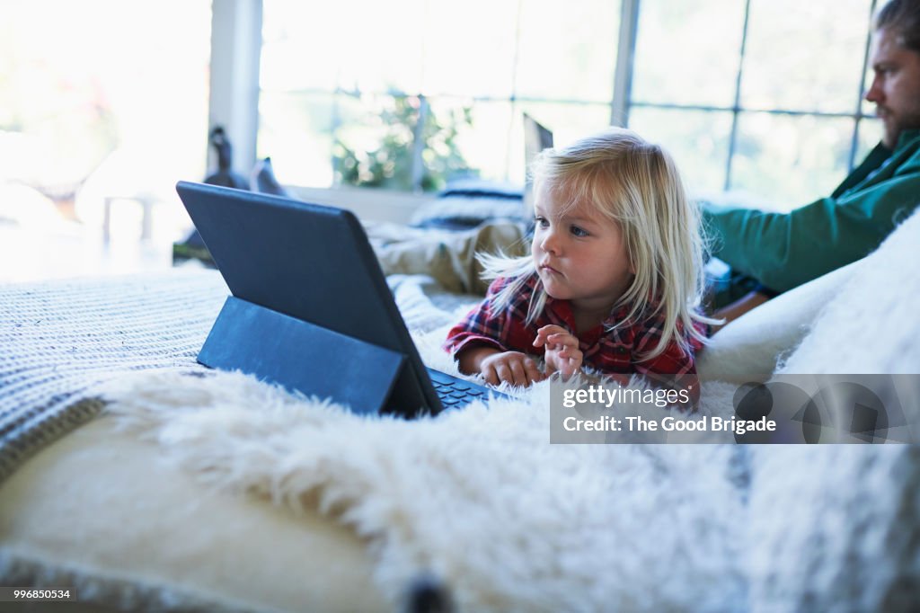 Father and daughter using technology on sofa at home