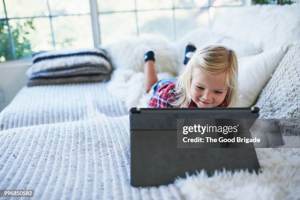 cute little girl using digital tablet while lying on sofa at home - sherman oaks fotografías e imágenes de stock