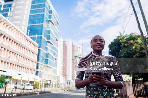 jeune fille africaine écouter de la musique sur les écouteurs de téléphone mobile dans le centre ville souriante - dar photos et images de collection