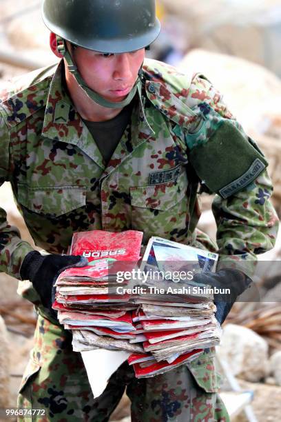 Self-Defense Force member recovers photos from mud as searching operation continues on July 11, 2018 in Kurashiki, Okayama, Japan. The death toll...