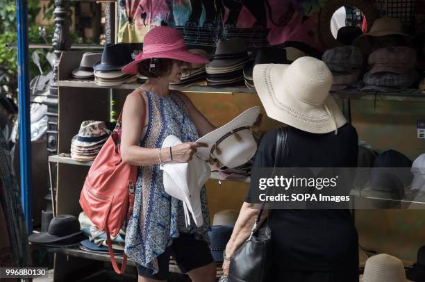 Women seen trying on different hats at a tourist shop. Tourists are shopping at Monastiraki in Athens. Its Summer sales season in Greece.