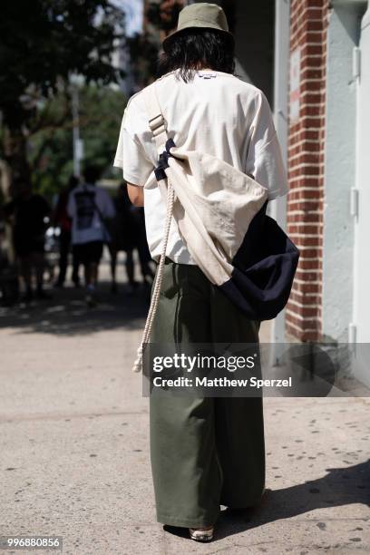 Guest is seen on the street during Men's New York Fashion Week wearing cream shirt and bag with army green pants on July 11, 2018 in New York City.