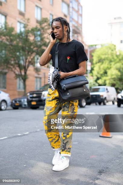 Guest is seen on the street during Men's New York Fashion Week wearing black shirt and bag with yellow camo pants on July 11, 2018 in New York City.