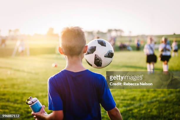 11 year old boy juggling soccer ball while walking off soccer field - calcio di squadra foto e immagini stock