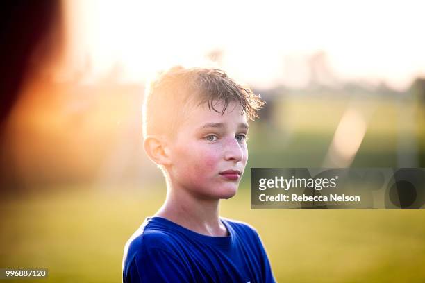 sweaty 11 year old boy watching teammates playing soccer from sidelines - spielfeldgrenze stock-fotos und bilder