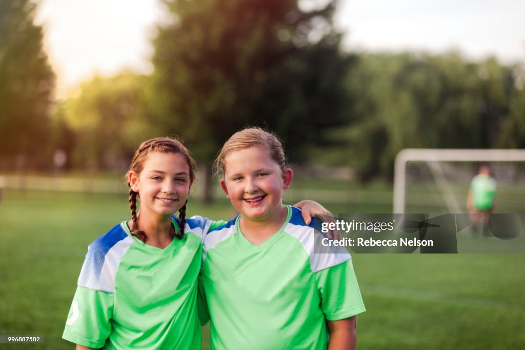 Two female soccer teammates with their arms around each other on soccer field