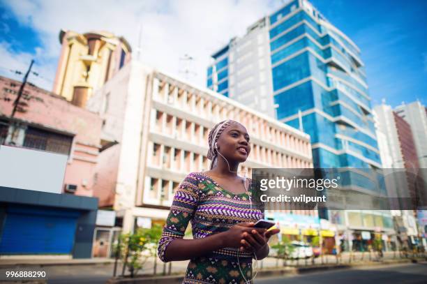 年輕的內容非洲女孩聽音樂從手機在市中心的耳機 - dar 個照片及圖片檔