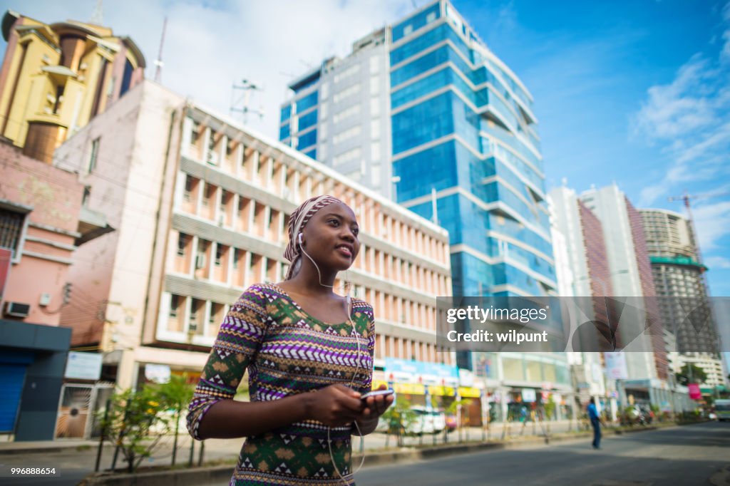 Young African Girl listening to music on earphones from Mobile Phone in the city centre