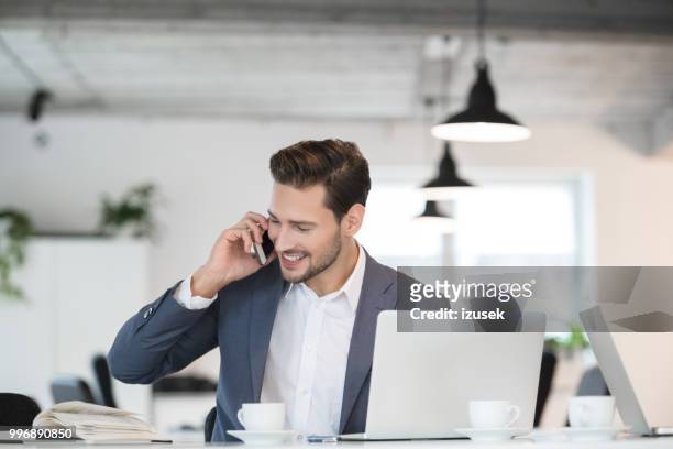 sonriente joven empresario trabajando en oficina - izusek fotografías e imágenes de stock
