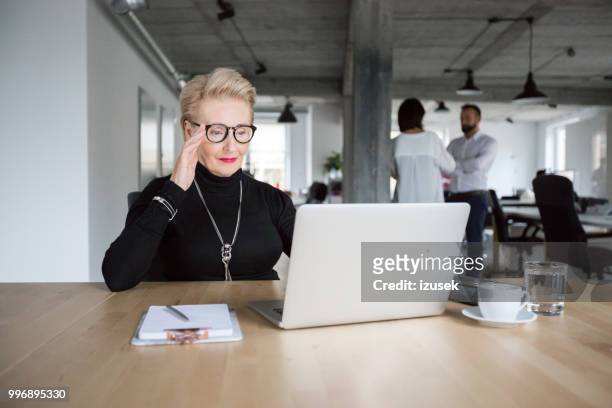 senior zakenvrouw die op laptop werkt - izusek stockfoto's en -beelden