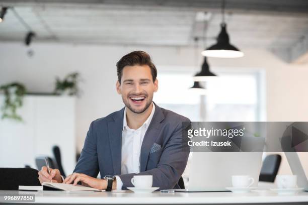 hombre de negocios guapo riéndose de su escritorio - izusek fotografías e imágenes de stock