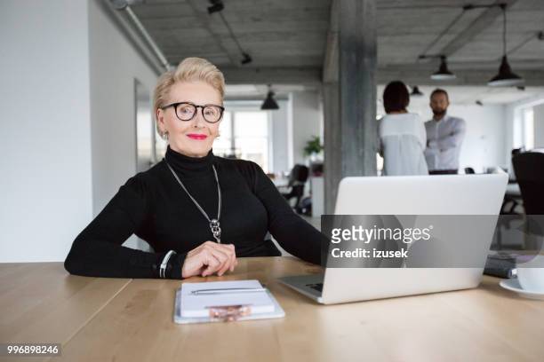 empresaria senior sentado en su escritorio - izusek fotografías e imágenes de stock