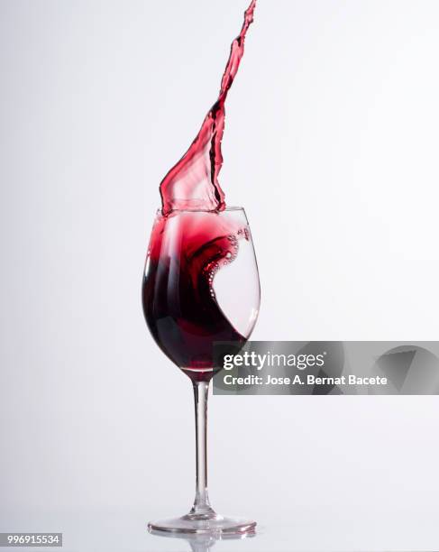 red wine splashing in glass in front of white background - kurzzeitfotografie stock-fotos und bilder